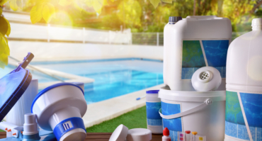 Swimming pool service and equipment with pool background Swimming pool service and equipment with chemical cleaning products and tools on wood table and pool background. Horizontal composition. Front view